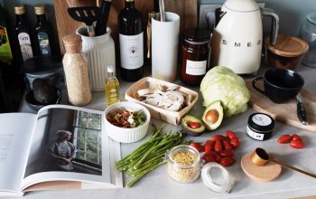 Various colorful healthy food and vegetables locating on countertop next to many different utensils and white kettle during cooking in stylish kitchen