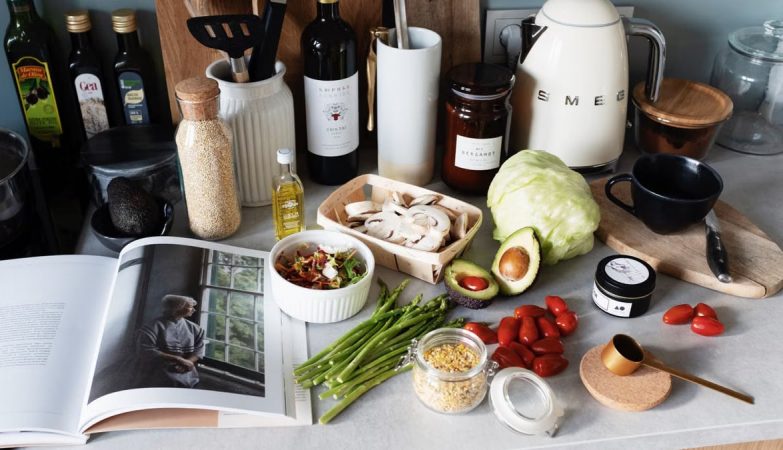 Various colorful healthy food and vegetables locating on countertop next to many different utensils and white kettle during cooking in stylish kitchen