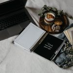 A cozy flat lay of a laptop, journals, and snacks on a bed for a relaxed work-from-home setup.