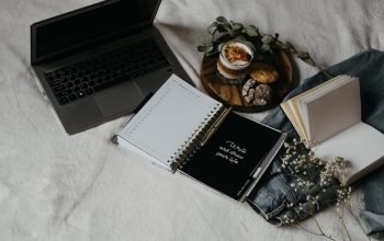 A cozy flat lay of a laptop, journals, and snacks on a bed for a relaxed work-from-home setup.