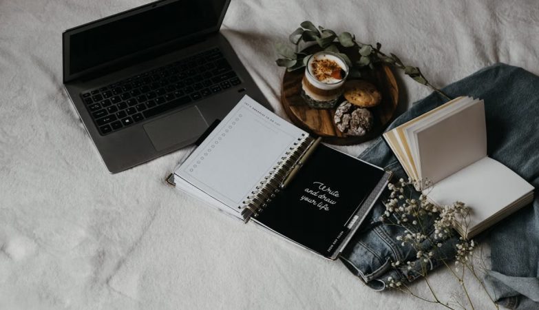 A cozy flat lay of a laptop, journals, and snacks on a bed for a relaxed work-from-home setup.